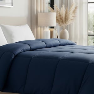 May include: A navy blue comforter with a quilted pattern is spread over a bed with white pillows. The bed is in a well-lit room with a neutral color palette, creating a serene and inviting atmosphere.