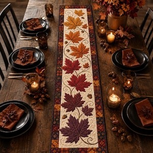 May include: A rectangular table runner featuring a cream-colored center panel decorated with an embroidered vine pattern and a gradient of autumn maple leaves transitioning from yellow and orange to deep red and purple, bordered by a plaid fabric.