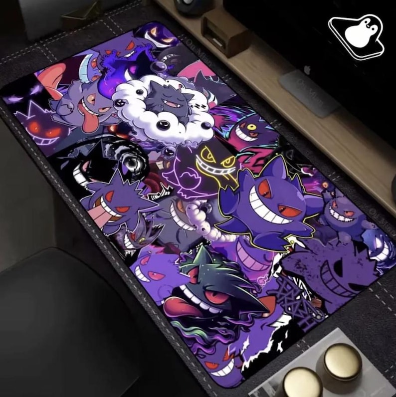 May include: A rectangular mouse mat with a collage of purple and black cartoon characters with red eyes and wide smiles. The design includes various shapes and sizes of the characters, creating a playful and dynamic look. The mouse mat is on a dark grey surface.