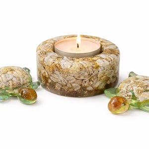 Peut inclure: Une tasse en céramique blanche avec une anse noire et le texte "But First, Coffee" en gras noir. La tasse est posée sur un fond flou, suggérant un cadre chaleureux.