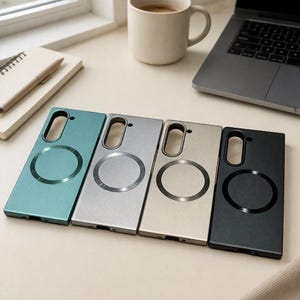 May include: Four phone cases in teal, silver, beige, and black, each with a circular magnetic ring and a camera cutout. The cases are rectangular and have a matte finish. A laptop, coffee cup, and notebook are in the background.