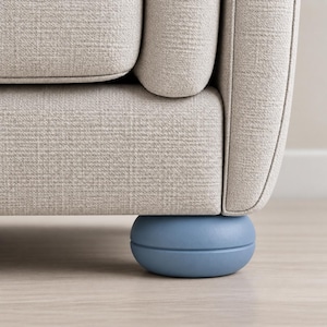 May include: A light beige upholstered sofa featuring a textured fabric finish and a rounded, matte light blue furniture leg. The leg has a smooth, circular, disc-like shape with a horizontal seam running through the center of its profile.