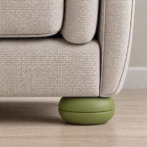 May include: A beige textured fabric sofa corner featuring a rounded, olive green furniture leg. The leg has a smooth, matte finish and a distinct horizontal seam running around its center, providing a contrast to the neutral woven upholstery.