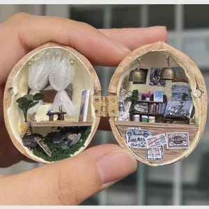 May include: A miniature diorama inside a hinged walnut shell. The left side features white curtains, a small table, and a green plant. The right side displays shelves with tiny books, two hanging bells, and labels reading Ford Motor, Signature, and Flag & Anthem.