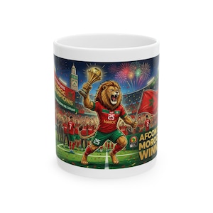 May include: White ceramic mug featuring a vibrant illustration of a lion in a soccer uniform holding a trophy. The design includes the Moroccan flag, text that reads "AFCON Morocco Winners", and a stadium scene with fireworks.