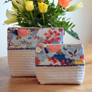 May include: Two zippered pouches with a floral print. The larger pouch is light beige with a blue and red floral print. The smaller pouch is light beige with a blue and red floral print. Both pouches have a zipper closure and a tassel pull.