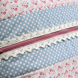 K&ouml;nnte beinhalten: Nahaufnahme eines Kissens mit Rei&szlig;verschluss und Spitzenbesatz. Das Kissen besteht aus Patchwork-Stoff mit einem blau-wei&szlig;en Punkte-Muster, einem rosa-wei&szlig;en Blumenmuster und einem wei&szlig;-rosa gestreiften Muster.