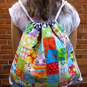 May include: A colourful patchwork drawstring backpack with a white drawstring. The backpack is made of various fabrics with different patterns, including polka dots, stripes and floral designs.