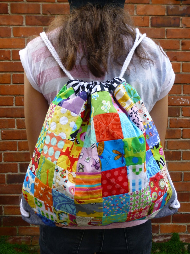 May include: A colourful patchwork drawstring backpack with a white drawstring. The backpack is made of various fabrics with different patterns, including polka dots, stripes and floral designs.