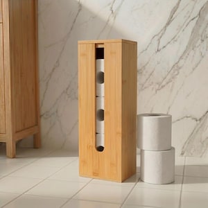 Puede incluir: Un soporte para papel higiénico alto y rectangular de bambú con una ranura vertical en la parte frontal. El soporte contiene tres rollos de papel higiénico blancos apilados, y hay otros dos rollos blancos apilados al lado.