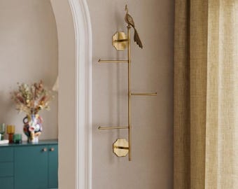 May include: A vertical brass wall-mounted rack featuring a central rod with three horizontal arms extending to the sides. The top of the rack is adorned with a detailed brass peacock figurine. The structure is secured to the wall by two octagonal plates.
