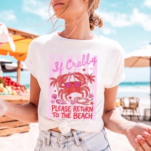 May include: White t-shirt with a pink and red graphic. The graphic features a crab wearing sunglasses, palm trees, and the text "If Crabby Please Return To The Beach."