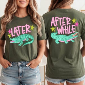 May include: Olive green t-shirt with a teal alligator graphic and the word "LATER" in pink, with yellow stars. The back of the shirt has the words "AFTER WHILE" in pink with a teal alligator and yellow and pink stars.