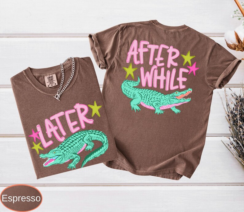 Puede incluir: Dos camisetas color espresso con dise&ntilde;os a juego. Una camiseta presenta el texto "LATER" y la otra "AFTER WHILE", ambas en rosa, con un caim&aacute;n verde y detalles de estrellas. Una cadena de plata est&aacute; en una camiseta.
