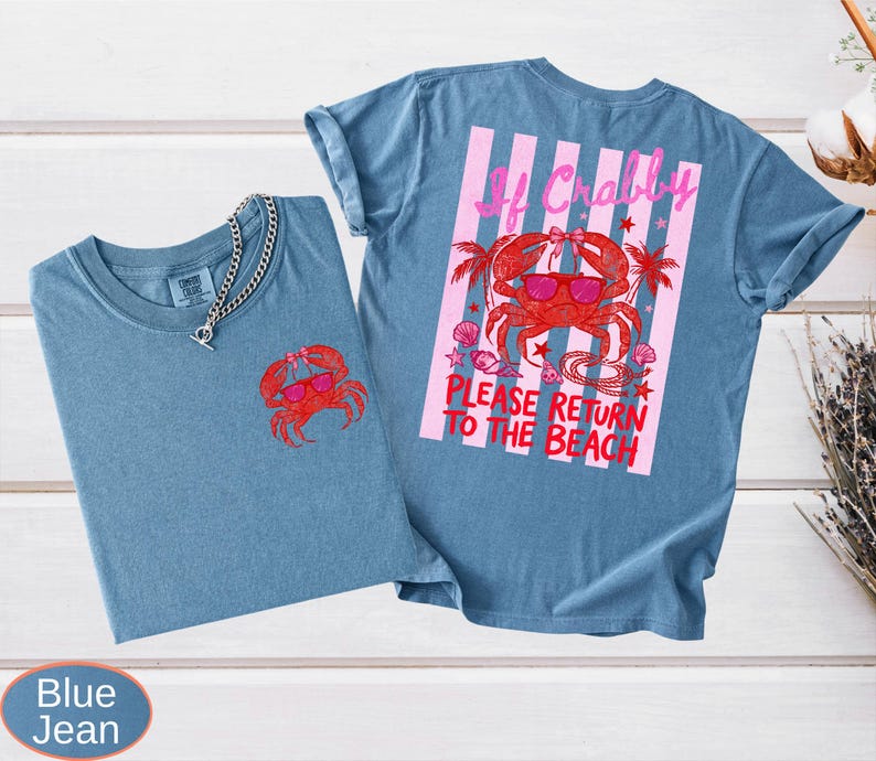 May include: Two blue jean t-shirts. One shirt has a red crab graphic on the front. The other shirt has a larger crab graphic on the back with the text "If Crabby, Please Return to the Beach" in pink and red.
