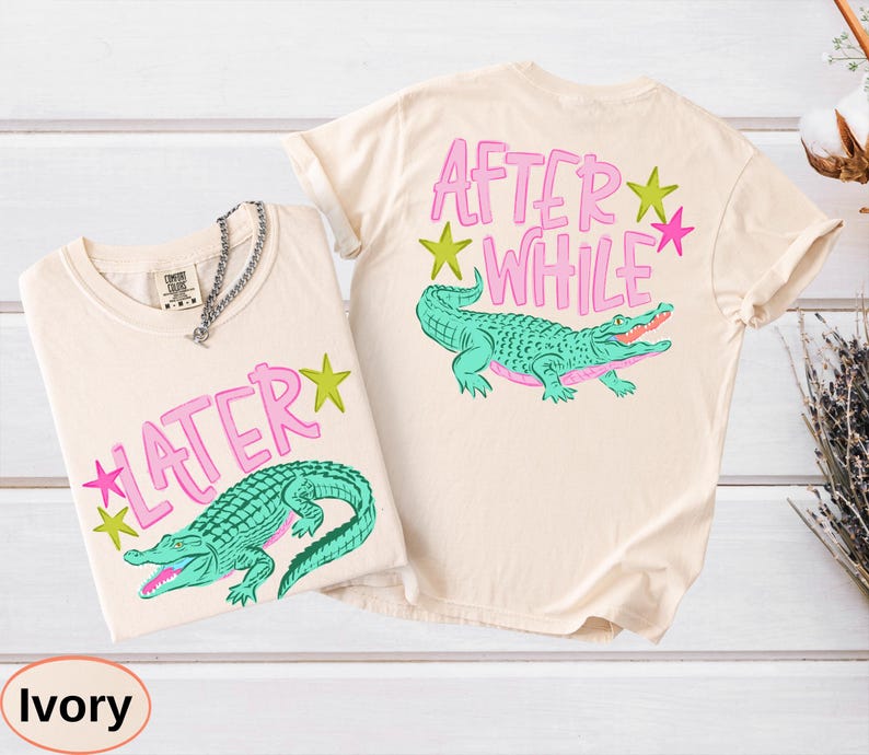 Puede incluir: Dos camisetas color marfil con dise&ntilde;os de caimanes. Una camiseta dice "LATER" con una estrella rosa, y la otra dice "AFTER WHILE" con una estrella rosa. Los caimanes son turquesas con detalles rosas.