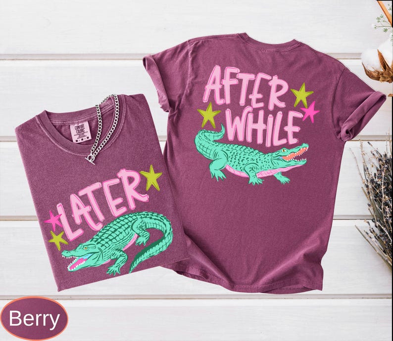 Puede incluir: Dos camisetas color bayas con dise&ntilde;os gr&aacute;ficos. Una camiseta presenta el texto "LATER" con un caim&aacute;n verde y estrellas. La otra camiseta tiene "AFTER WHILE" con un caim&aacute;n y estrellas.