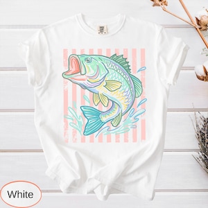 Puede incluir: Camiseta blanca con una ilustraci&oacute;n colorida de un pez saltando. El pez est&aacute; representado en tonos de azul, verde, amarillo y rosa, sobre un fondo a rayas rosas y blancas. La camiseta es de estilo casual.