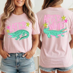 May include: Pink t-shirts with a teal alligator graphic and text. The front of the shirt says "LATER" with a star, and the back says "AFTER WHILE" with a star. The shirts are worn by a person.