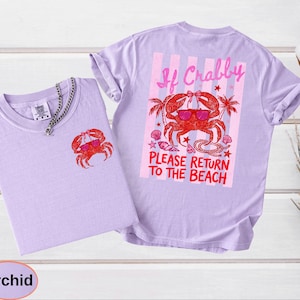 May include: Two orchid-colored t-shirts with a crab graphic. One shirt has a small crab on the front, and the other has a larger crab design on the back with the text "If Crabby, Please Return to the Beach". The crab is wearing sunglasses.