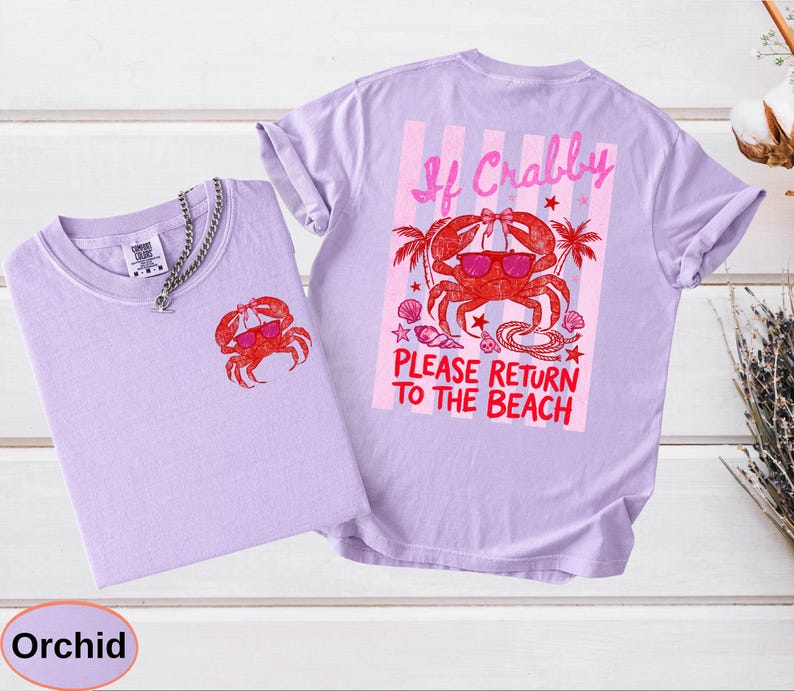 May include: Two orchid-colored t-shirts with a crab graphic. One shirt has a small crab on the front, and the other has a larger crab design on the back with the text "If Crabby, Please Return to the Beach". The crab is wearing sunglasses.