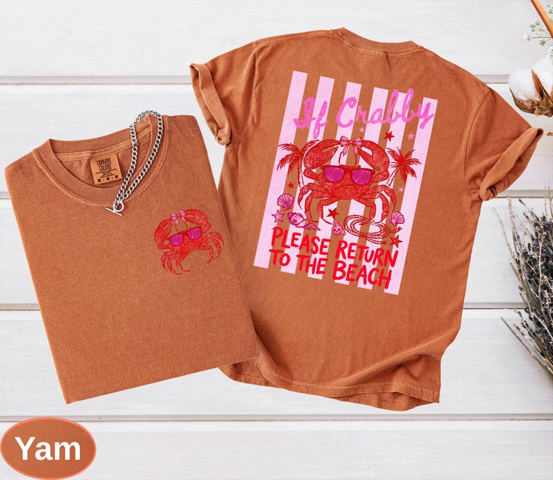 May include: Two yam-colored t-shirts with a crab graphic. One shirt has a small crab design on the front, and the other has a larger crab design with text that reads "If Crabby, Please Return to the Beach". A silver chain necklace is on the front shirt.