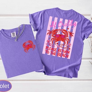 May include: Two violet t-shirts with a crab graphic. One shirt has a small crab on the front, the other has a larger crab design on the back with text that reads "If Crabby, Please Return to the Beach."