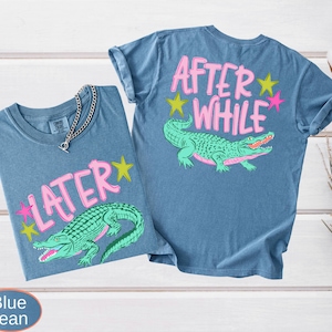 Puede incluir: Dos camisetas azul vaquero con un gr&aacute;fico de un caim&aacute;n verde y las palabras "LATER" y "AFTER WHILE" en rosa. El caim&aacute;n tiene una boca rosa y est&aacute; rodeado de estrellas amarillas y rosas. Una cadena de plata est&aacute; en una camiseta.