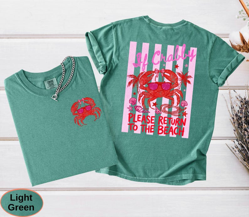 May include: Two light green t-shirts. One shirt has a small red crab graphic on the front. The other shirt has a larger crab graphic with sunglasses and the text "If Crabby Please Return to the Beach" on the back.