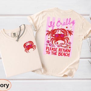 May include: Ivory-colored t-shirts with a crab graphic. One shirt has a small crab on the front, the other has a larger crab design with text that reads "If Crabby, Please Return to the Beach".