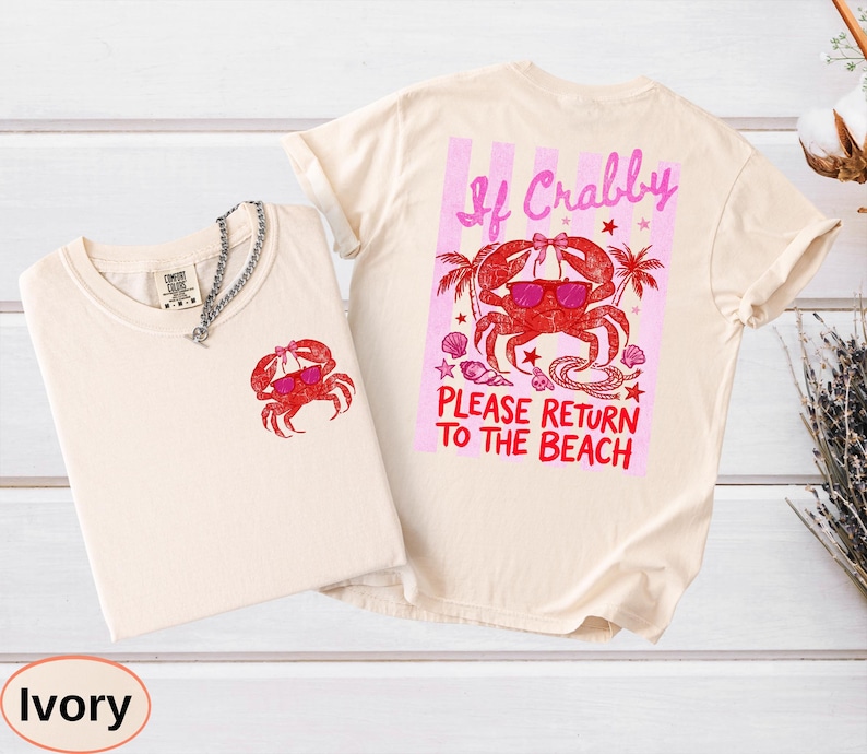 May include: Ivory-colored t-shirts with a crab graphic. One shirt has a small crab on the front, the other has a larger crab design with text that reads "If Crabby, Please Return to the Beach".