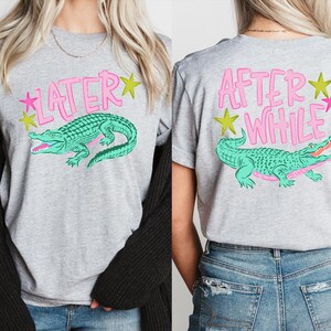 May include: Gray t-shirt with a teal alligator graphic and the text "LATER" on the front and "AFTER WHILE" on the back, with pink and yellow star accents. The shirt is a casual style.
