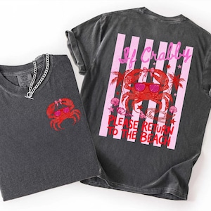 May include: Two dark gray t-shirts with a red crab graphic wearing sunglasses. One shirt has the crab on the front, the other has a crab graphic with text that reads "If Crabby, Please Return to the Beach" on the back. A silver chain necklace is on one shirt.