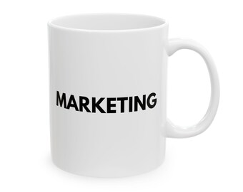 May include: A white ceramic mug featuring the word MARKETING printed in bold black capital letters on the front. The mug has a smooth, cylindrical body and a curved handle on the right side, providing a clean and simple design for daily use.