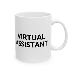 May include: A white ceramic mug featuring the text VIRTUAL ASSISTANT printed in bold black capital letters on the front. The mug has a smooth, glossy finish, a cylindrical body, and a curved handle on the right side for holding the vessel.