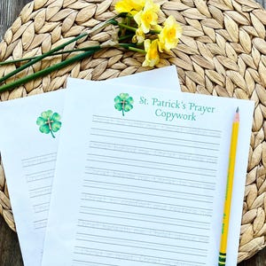 May include: Two sheets of white paper with the text "St. Patrick's Prayer Copywork" and a shamrock graphic. A yellow pencil rests on the paper. Yellow daffodils and green stems are in the background. The papers have lined spaces for writing.