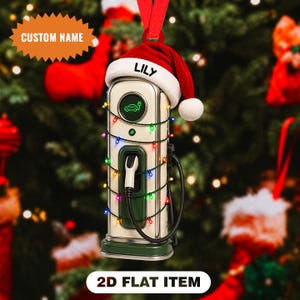 May include: A 2D flat ornament shaped like an electric vehicle charging station, featuring a cream and green body, a charging cable, and a red Santa hat with the name LILY printed on the white brim. The station is wrapped in colourful string lights.
