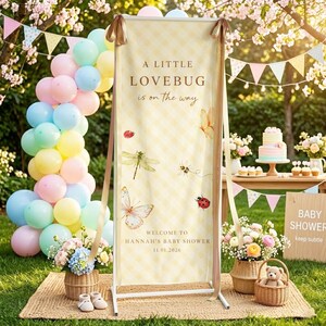 May include: A baby shower banner with the text "A Little Lovebug is on the way." The banner is decorated with butterflies, dragonflies, and ladybugs. The words "Welcome to Hannah's Baby Shower 11.01.2026" are also displayed.