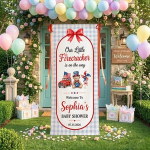 May include: A baby shower banner with a red bow and the text "Our Little Firecracker is on the way." The banner features a red truck, a teddy bear, and a pinwheel. The banner says "Welcome to Sophia's Baby Shower" and the date 07.15.2026.