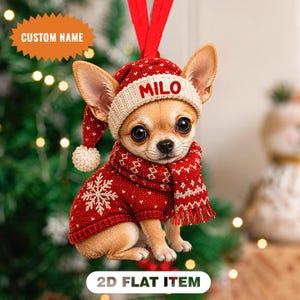 Könnte beinhalten: Ein flaches 2D-Hängeornament, das einen beigen Chihuahua zeigt, der einen rot-weißen Strickpullover, einen passenden roten Schal mit weißen Mustern und eine rot-weiße Strickmütze mit dem Namen Milo in roter Schrift auf dem Rand trägt.