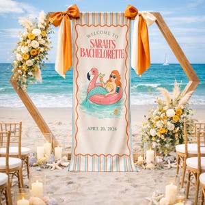 May include: A beach-themed bachelorette party banner with the text "Welcome to Sarah's Bachelorette" and the date April 20, 2026. The banner features a cartoon illustration of a mermaid on a flamingo float. The scene includes floral arrangements, candles, and a wooden arch.