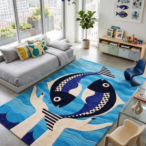 Pode incluir: Um tapete retangular com um padrão de água ondulada em azul vibrante e dois grandes peixes estilizados em azul escuro e branco. O design inclui duas grandes mãos de cor creme que se estendem para cima a partir da borda inferior.