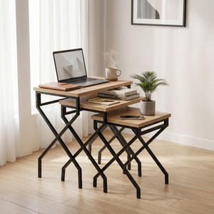 Könnte beinhalten: Ein Satz von drei Beistelltischen mit hellen Holzplatten und schwarzen Metallbeinen in X-Form. Ein Laptop, eine Tasse, Bücher und eine Topfpflanze stehen auf den Tischen. Die Tische befinden sich in einem Heimbüro in der Nähe eines Fensters.
