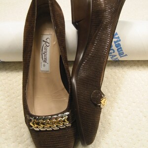 May include: A pair of brown suede flats with a textured pattern. The shoes feature a gold and silver chain detail across the top and a small heel. The brand name "Rangoni" is visible inside one shoe.