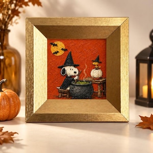 May include: A square framed artwork featuring a textured orange background with a black witch hat-wearing Snoopy stirring a black cauldron. A small yellow bird wearing a witch hat sits on a white pumpkin nearby, with a yellow moon and black bats above.