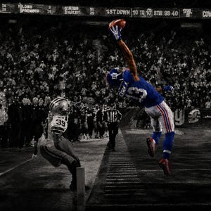 May include: A football player in a blue jersey with the number 13 and white shorts leaps high to catch a brown football. A second player in a white uniform with the number 39 stands nearby on a dark pitch with a blurred crowd in the background.