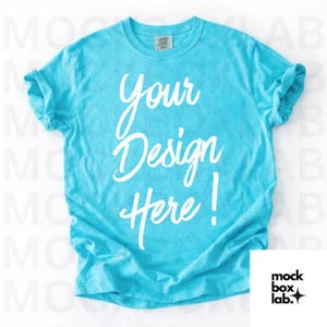 May include: A turquoise t-shirt with rolled-up sleeves. The shirt features the white text "Your Design Here!" in a cursive font. The mock box lab logo is in the bottom right corner.