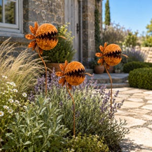 Può includere: Tre picchetti da giardino in metallo color ruggine a forma di piante sferiche dentate con petali appuntiti. Ogni scultura presenta una testa rotonda e strutturata con una bocca aperta frastagliata e un sottile stelo in metallo.