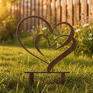 May include: A rustic metal heart sculpture for garden decoration. The sculpture has two intertwined hearts with a weathered, brown finish. It is mounted on a rectangular base with two short legs, designed to be placed in the grass.