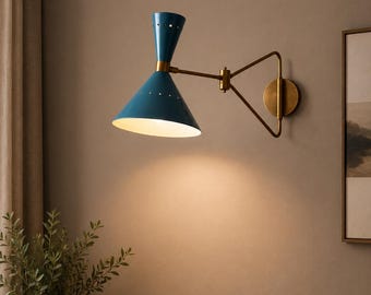 May include: A wall-mounted lamp featuring a dual-cone teal shade with small circular perforations near the centre. The fixture has a brass-toned articulated arm and a circular wall plate, casting a warm light downward from the cone-shaped head.